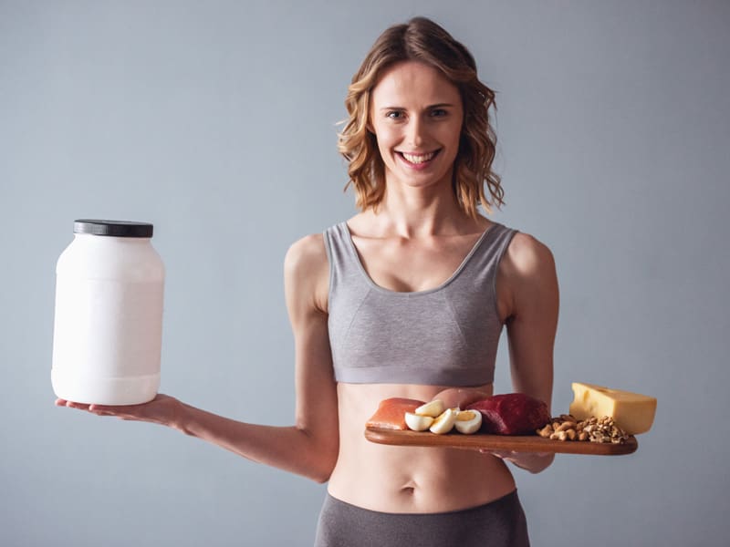 woman holding good protein food and also protein powder to illustrate protein intake needs