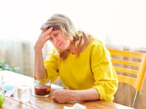 mature woman with pills and cup of tea looking unwell to illustrate inflammation and aging