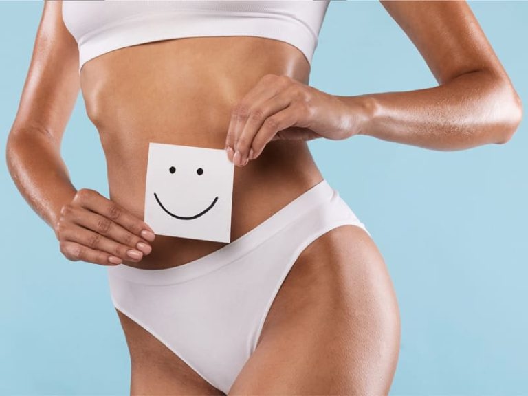 Woman holding paper smiley in front of her toned body to illustrate the benefits of Emsculpt Neo treatment