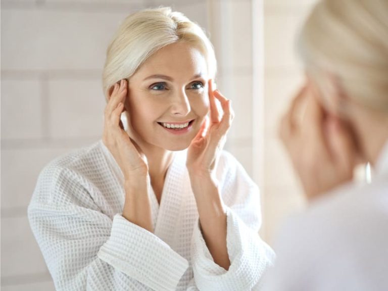 woman with glowing skin looking happily in the mirror - to illustrate the effects of Niagen IV therapy