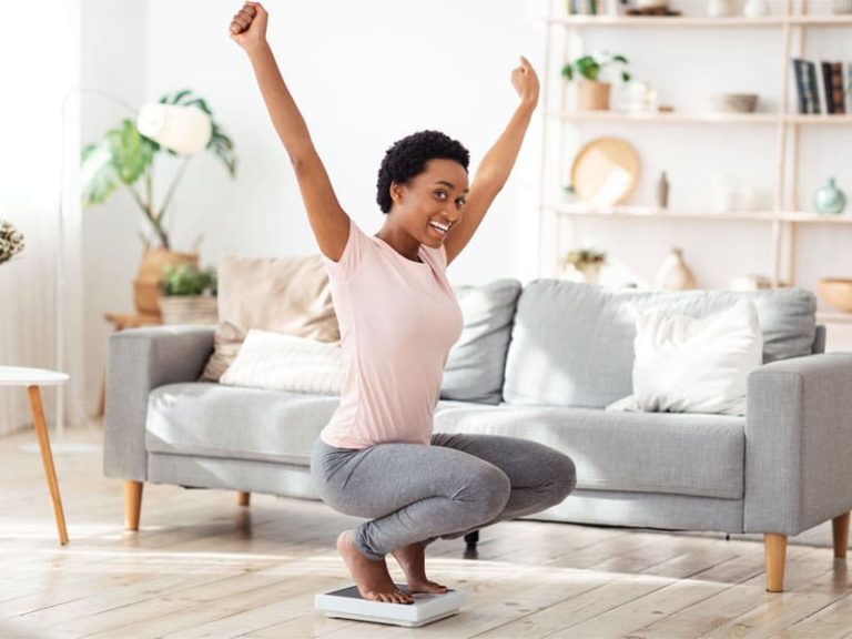 young woman sitting on scales with arms raised to illustrate the success of semaglutide and weight loss