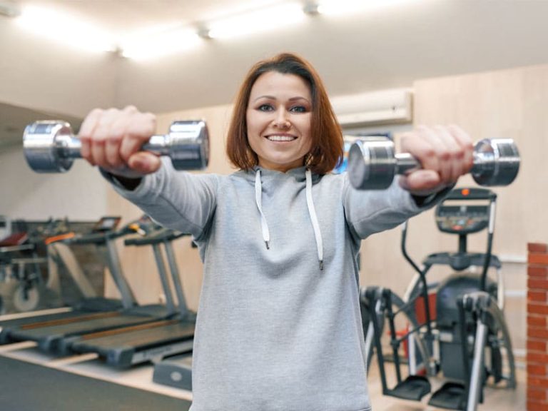 woman in gym using hand weights to illustrate does perimenopause cause weight gain