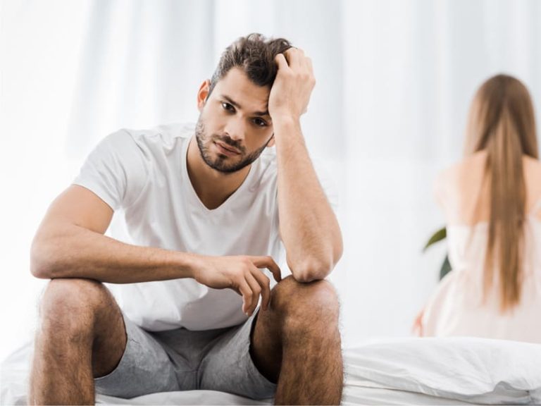 upset man sitting on bed to illustrate wondering does testosterone help with ED