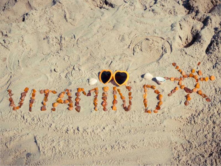 Pebbles on the sand reading "vitamin D" and a sun shape, to illustrate vitamin D3 injections