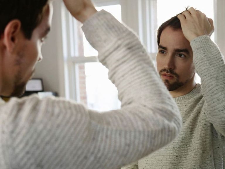 Man inspecting hair in mirror to illustrate thinking about PRP for hair loss
